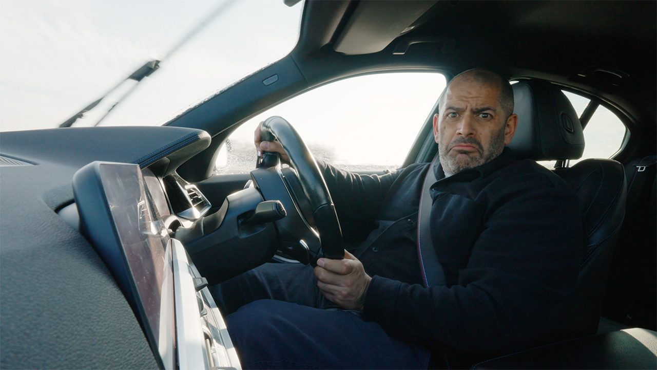 Chris Harris frowning at camera while driving car