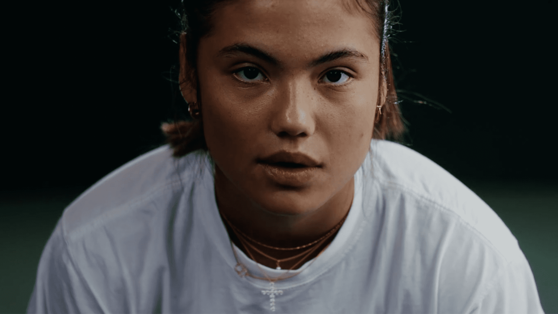 Tennis Professional, Emma Raducanu, stares directly at the camera in a white T-shirt