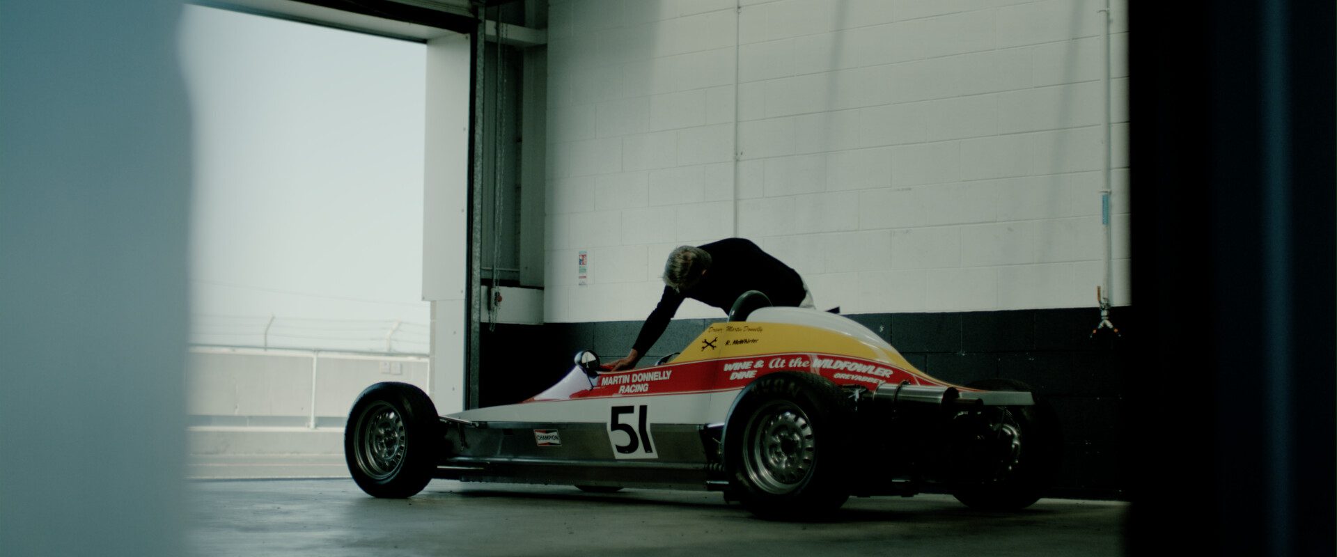 Man (Martin Donnelly) leans over to inspect vintage race car